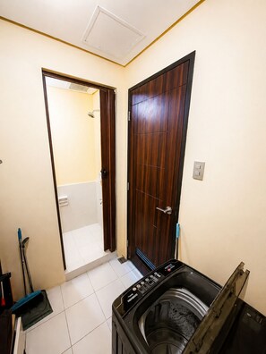 A laundry room with a washing machine, a mop, and a broom.