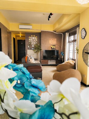 Un salon avec un canapé, un téléviseur à écran plat et une horloge murale.
