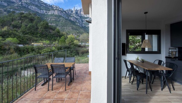 Un balcón con mesa y sillas, con vistas a un paisaje montañoso.