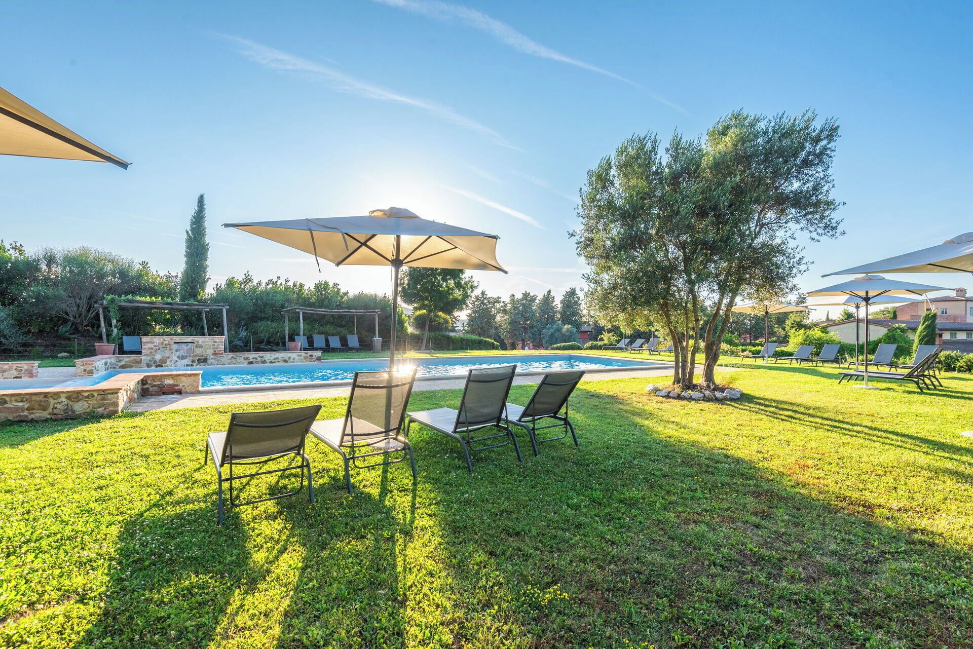 Un espace aménagé au bord de la piscine, avec des chaises longues et des parasols, entouré de verdure et d’un mur en pierre.