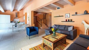 Un salon moderne comprenant un canapé, des fauteuils, une table basse et un escalier menant à la cuisine.