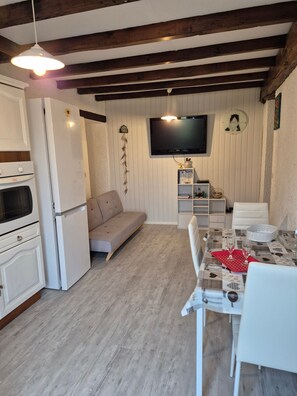 A cozy room with a dining table, chairs, a sofa, a TV, and a kitchen area with a fridge and oven. - Apartment 'Mamie Krema' with Private Terrace, Shared Garden and Wi-Fi (Boresse-et-Martron)