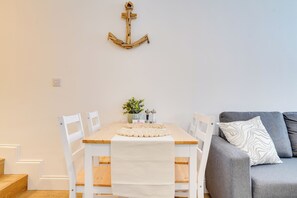 A dining area with a wooden table, white chairs, a white tablecloth, a small plant, and a wall-mounted anchor decoration. - Apt 1 Armatage Flats, Eyemouth (Eyemouth)