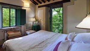 Ein Schlafzimmer mit Bett, Stuhl, Tisch mit Lampe und Fenster mit Blick auf Grünflächen.