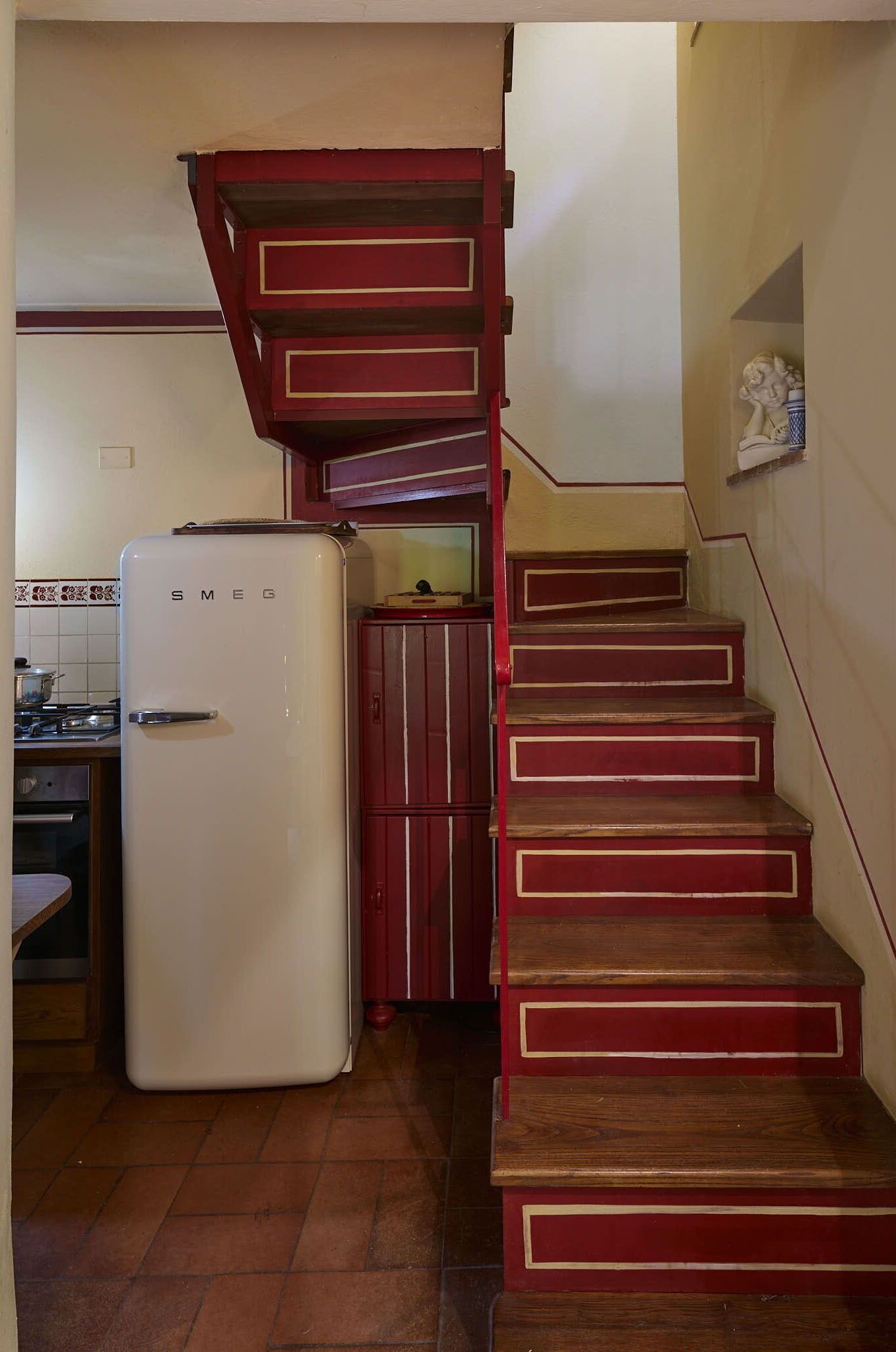 A kitchen with a white refrigerator, wooden stairs, and a red cabinet.