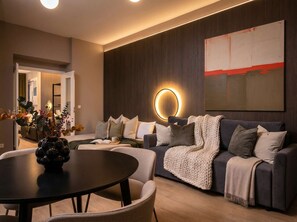 A modern living room with a dark grey sofa, a round coffee table, and a wall-mounted circular light. - TurnKey | Bright 2BR for Groups up to 12, Prague (Praha 2)