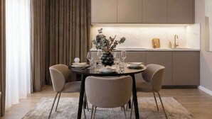 Un comedor moderno con una mesa redonda, cuatro sillas, un florero con follaje y una cocina al fondo.