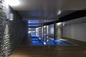Un espace piscine intérieur moderne, doté d’un plancher en bois, d’un mur en pierre et de rampes en métal.