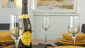 Una mesa de comedor con platos amarillos, una botella de Prosecco y dos copas.