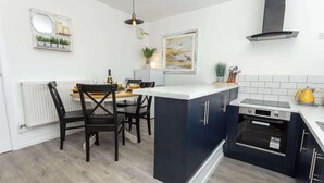 Una cocina moderna con una isla central, armarios oscuros, horno empotrado y encimera blanca.