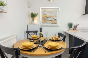 Ein Essbereich mit einem runden Tisch, gedeckt für vier Personen, mit gelben Schüsseln und Weingläsern, einer Champagnerflasche und schwarzen Platzsets.