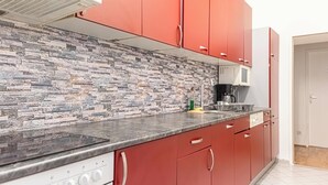 Une cuisine avec des meubles de couleur rouge, un pare-feu en pierre et une hotte de cuisson en acier inoxydable.