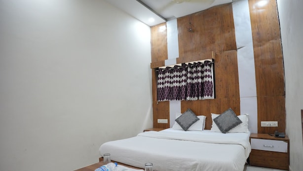 A hotel room with a bed, bedside table, nightstand, and a wall-mounted curtain. - HOTEL JAY BHAWANI (Ahmedabad)