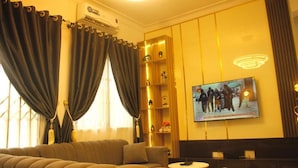 A modern living room with a sofa, a small round table, and a television mounted on the wall. - Monica Apartment (Abuja)