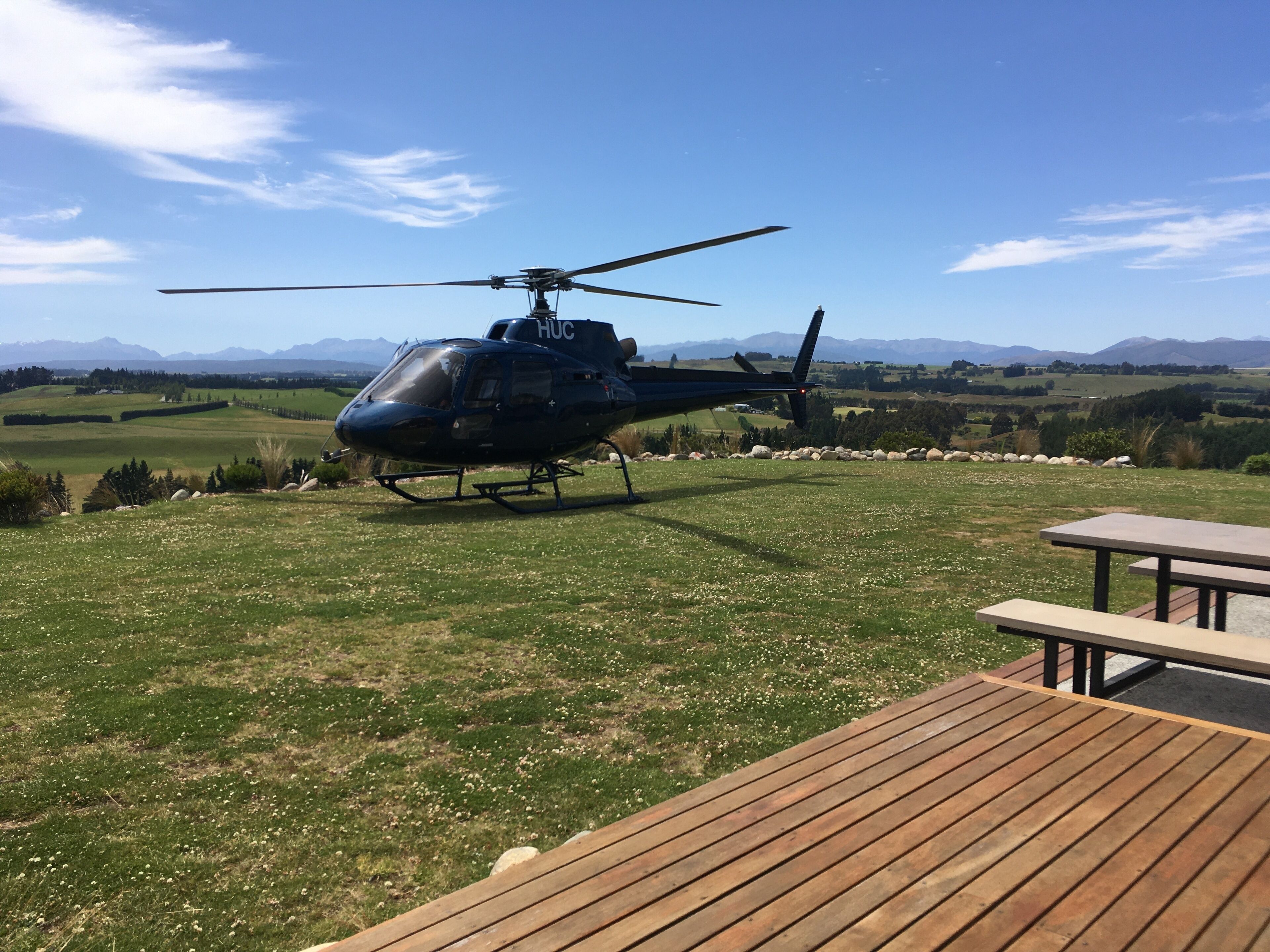 A helicopter parked on a grassy field with a picnic table in the foreground.