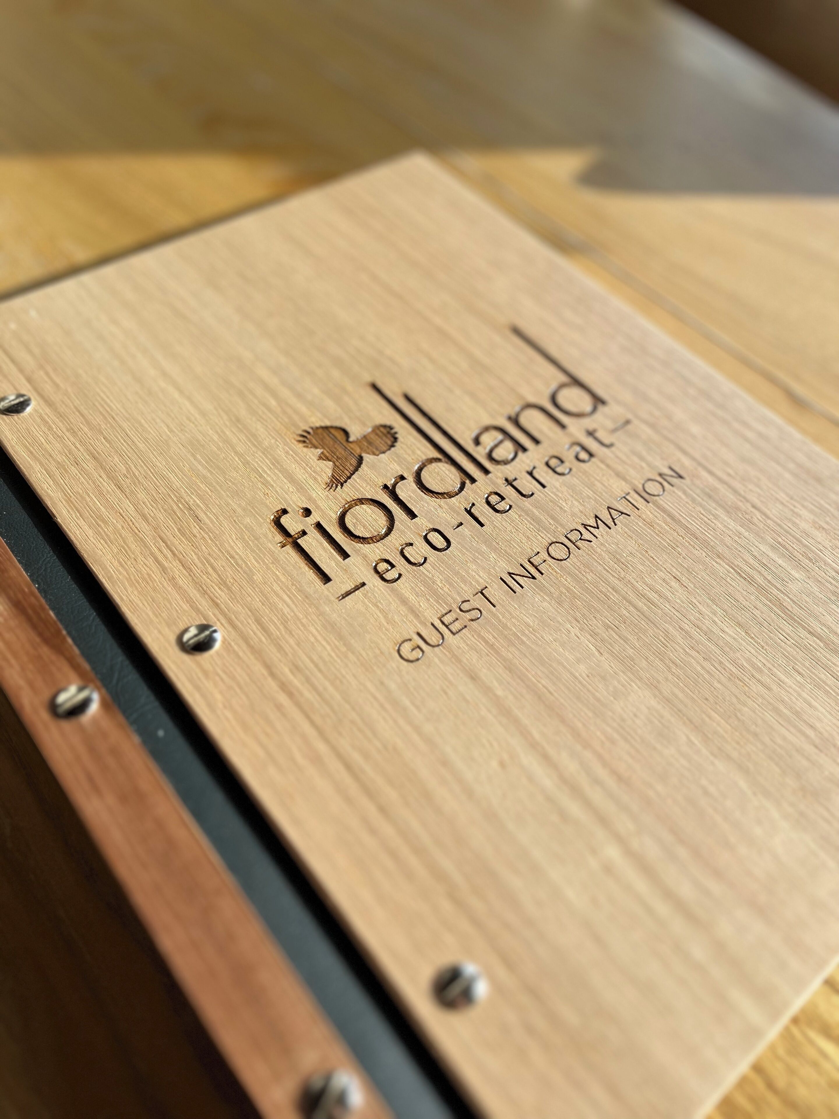 A wooden folder with embossed text and a bird logo, labeled "fiorland eco-retreat" and "GUEST INFORMATION".
