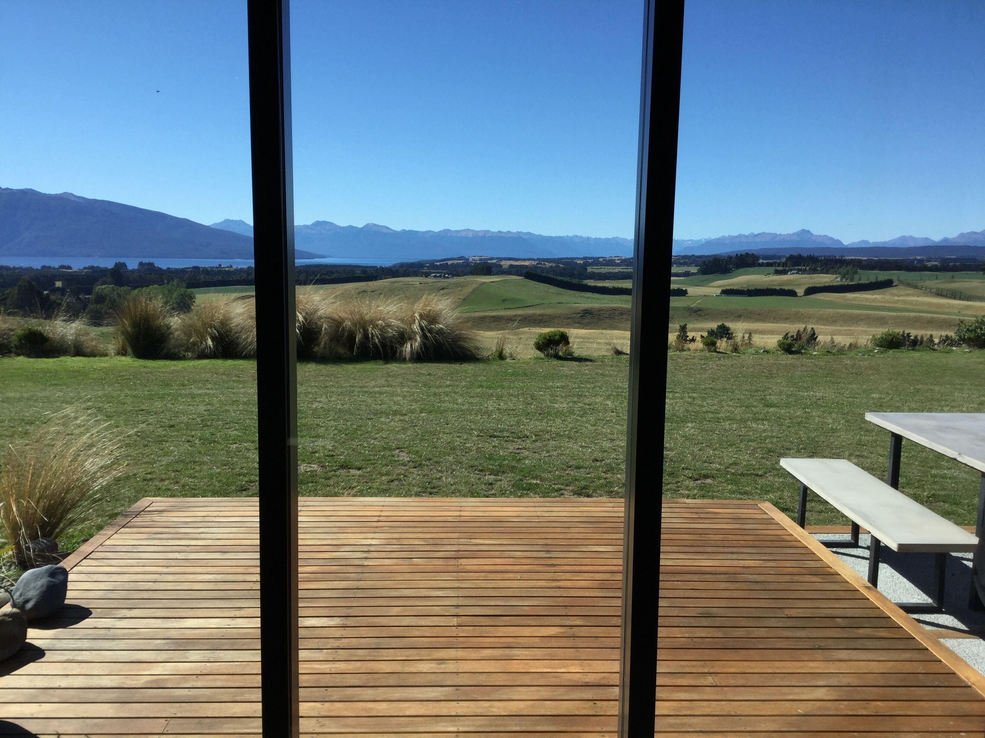A wooden deck with a bench and a table, overlooking a grassy landscape with rolling hills and distant mountains.