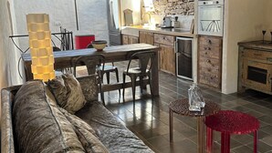 Ein gemütliches Wohnzimmer mit einer Couch, einem Esstisch und Stühlen. Es gibt eine Küchenzeile mit Kühlschrank, Herd und Schränken.