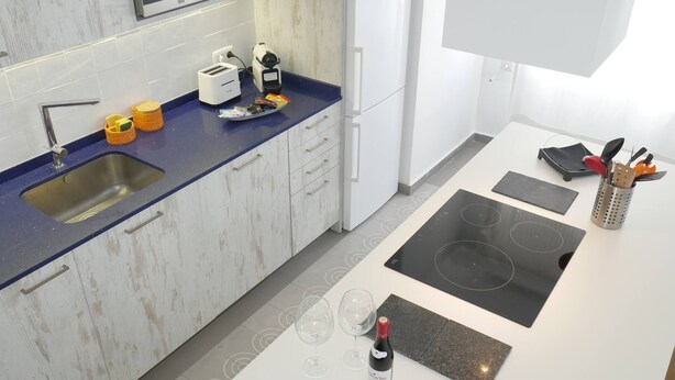 Een moderne keuken met een blauw aanrecht, een roestvrijstalen spoelbak, witte kasten en een geïntegreerd inductiefornuis.