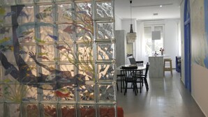 Een modern interieur met een glazen wand waarop kleurrijke vissen te zien zijn, een eethoek met een tafel en stoelen, en een keuken met een aanrecht en kasten.