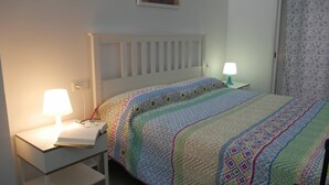 Een net opgemaakt bed met een kleurrijke quilt, een bedlampje en een boek op een nachtkastje.