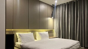 Una camera d'albergo moderna con un letto grande, una testata imbottita con illuminazione integrata e vista sulla città attraverso delle tende.