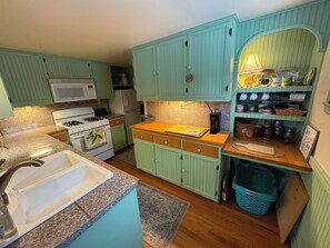 Une cuisine de taille réduite avec des meubles de couleur turquoise, une cuisinière à gaz, un four à micro-ondes et un évier.
