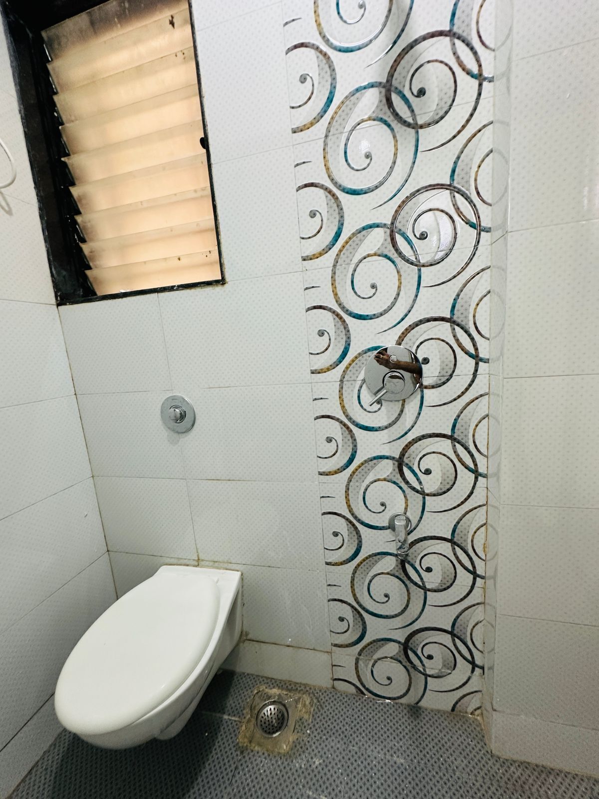 Ein kleines Badezimmer mit Fliesen, einer Toilette, einer Dusche und einem Abfluss.