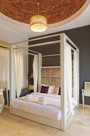 A four-poster bed with white linens and towels, a brick ceiling, and a chandelier. - Vesta - Luxury APT - 3BR - South Marina (El Gouna)