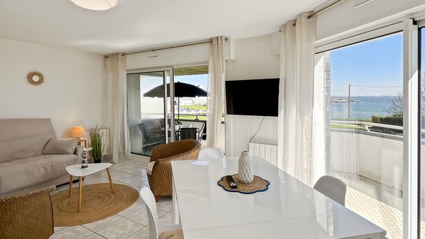 A modern living room with a sofa, dining table, chairs, and a TV. - Ploemeur T2 with Balcony, Garage 30m to Beach (Ploemeur)