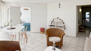 A modern living room with a dining area, a wicker chair, a white coffee table, and a view into another room. - Ploemeur T2 with Balcony, Garage 30m to Beach (Ploemeur)