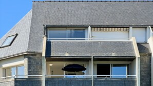 A two-story building with a grey brick facade, multiple windows, and a balcony with a black umbrella. - Ploemeur T2 with Balcony, Garage 30m to Beach (Ploemeur)
