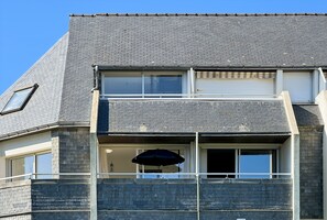 Ein zweistöckiges Gebäude mit einer grauen Ziegelaußenwand, zahlreichen Fenstern und einem Balkon mit einem schwarzen Sonnenschirm.