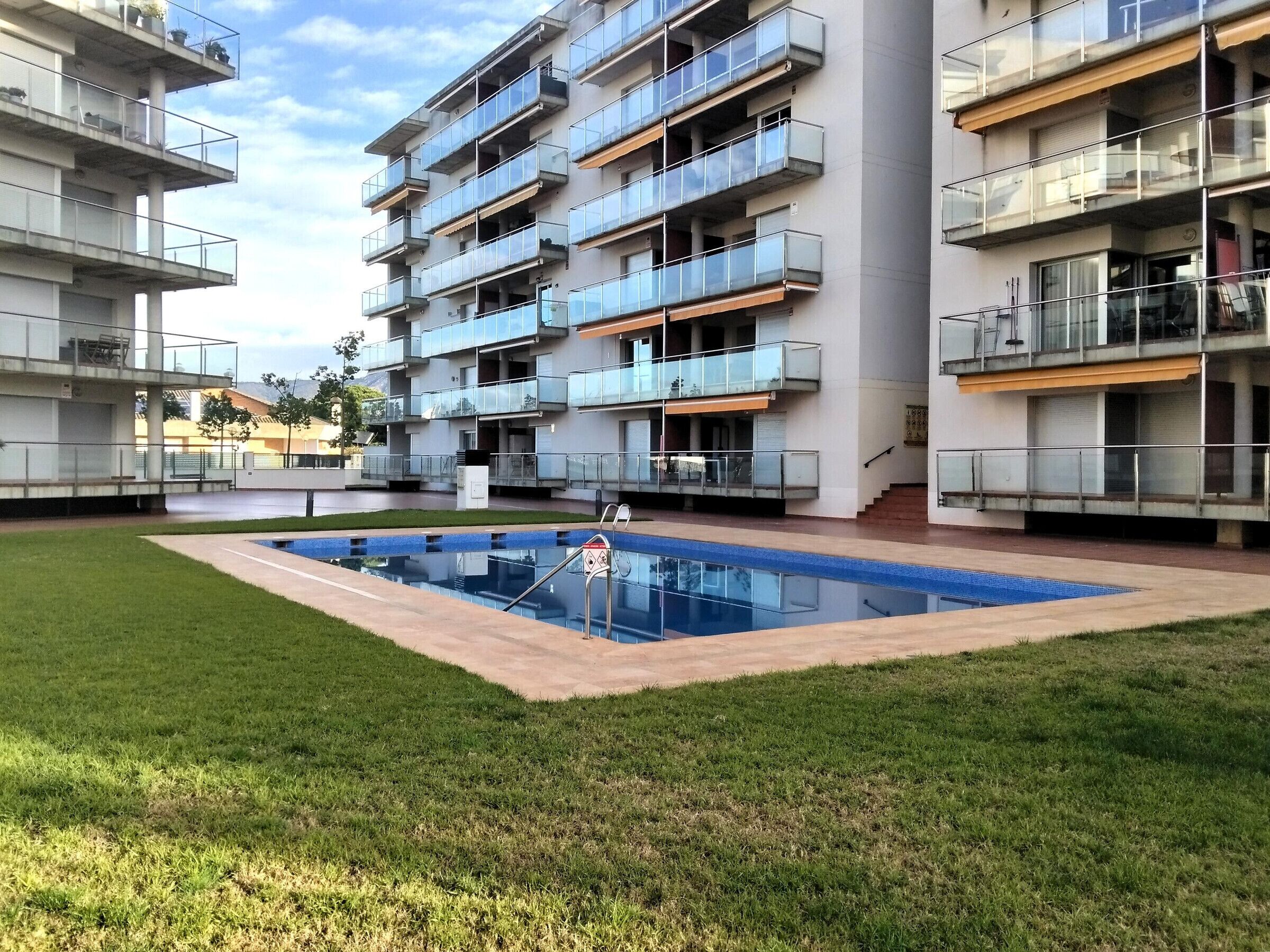 A multi-story residential building with balconies, a swimming pool, and a grassy courtyard.