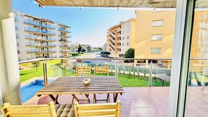 Ein Balkon mit Holztisch und Stühlen, Geländer aus Glas und Blick auf umliegende Gebäude.