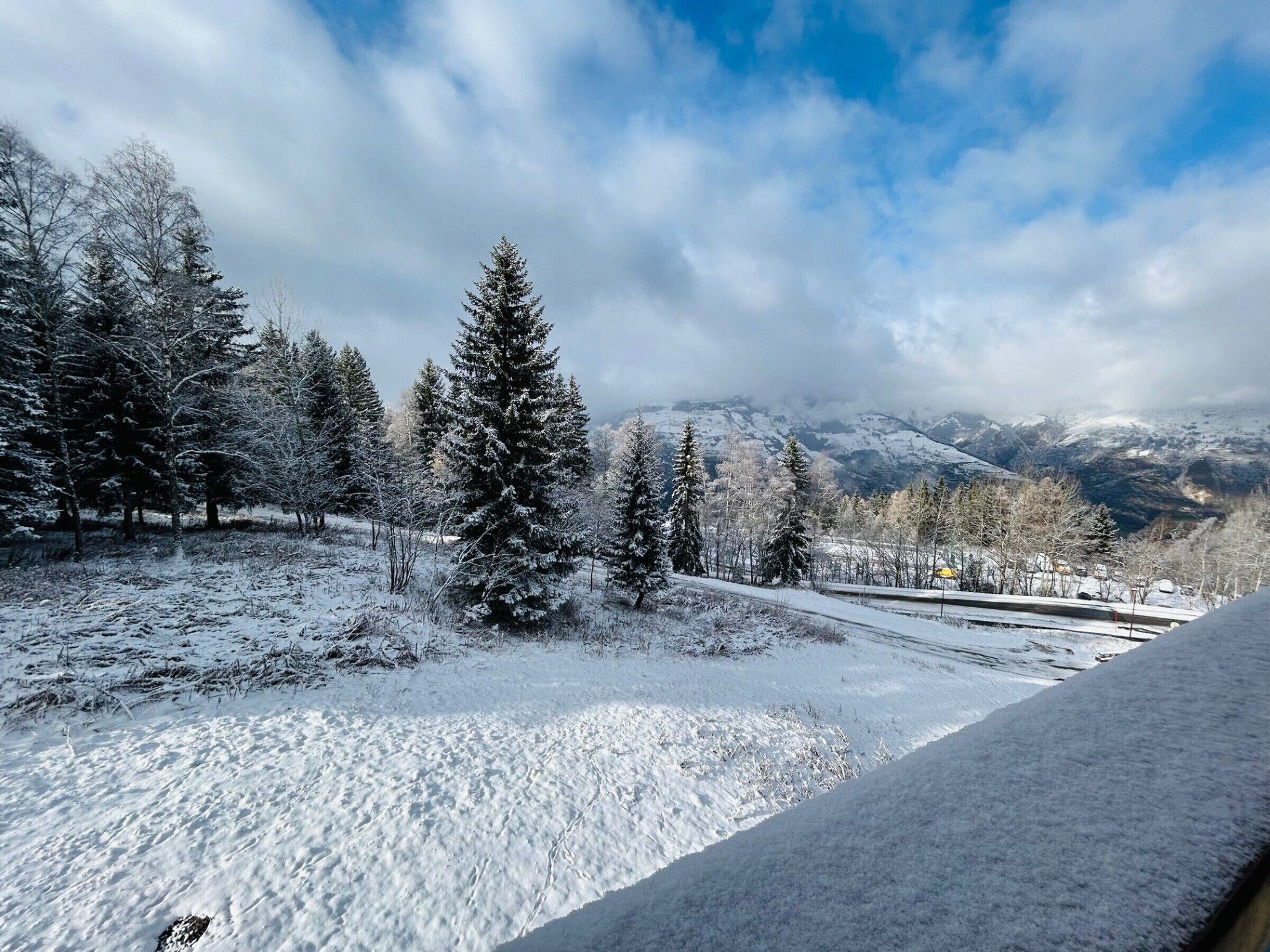 A snowy landscape with a clear sky, trees, and distant mountains.