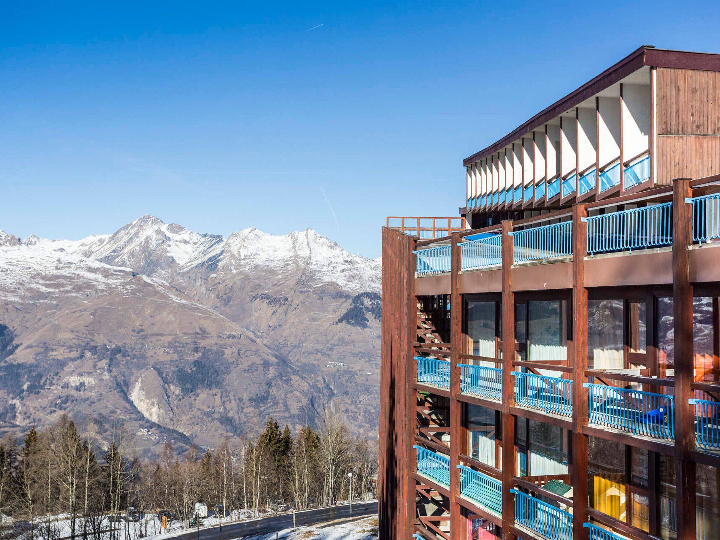Um edifício com várias andares e varandas, com montanhas cobertas de neve ao fundo.