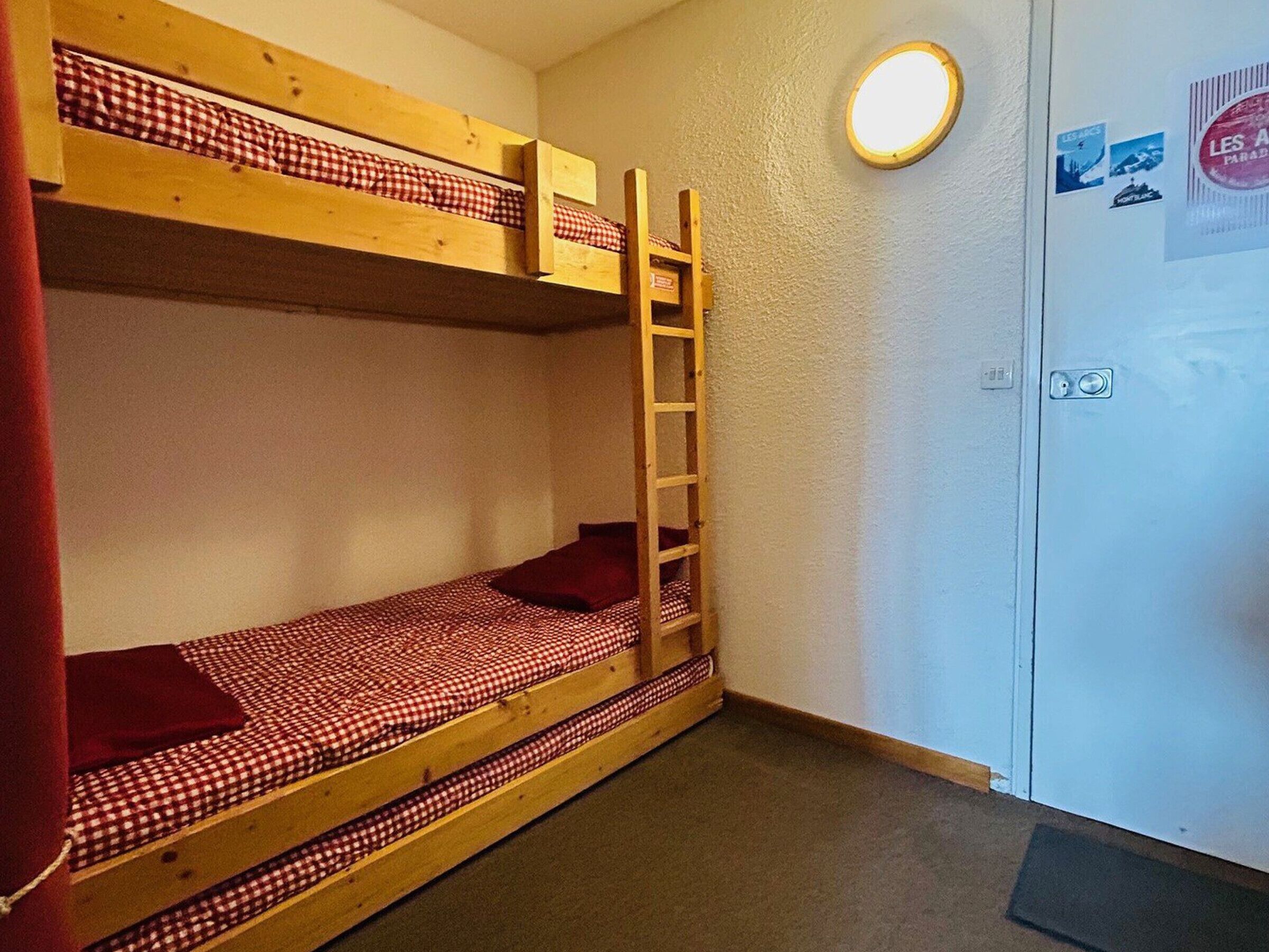 Une chambre avec un lit superposé, une échelle, une porte décorée d’autocollants et un luminaire rond.
