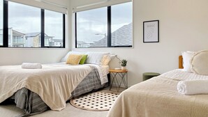 Une chambre moderne avec deux lits, de grandes fenêtres, un tapis rond et une petite table d’appoint.