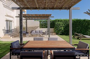 An outdoor patio with a wooden table and chairs, a covered seating area, and a lawn. - Vesta - Luxury Villa - 4BR - Joubal (El Gouna)