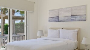 A bedroom with a large bed, a nightstand, a lamp, a view of the outdoors, and a painting on the wall. - Vesta - Luxury Villa - 4BR - Joubal (El Gouna)