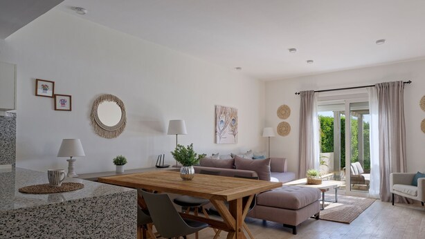 A modern living room with a wooden dining table, grey chairs, a sofa, and a coffee table. There are decorative items on the walls and a view of the outdoors through a glass door. - Vesta - Luxury Villa - 4BR - Joubal (El Gouna)