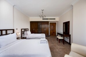 Quarto de hotel com duas camas, uma escrivaninha, uma cadeira, uma televisão e um guarda-roupa.