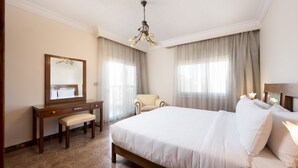 Une chambre d’hôtel avec un grand lit, un bureau en bois avec une banquette, une chaise, un miroir et un lustre.