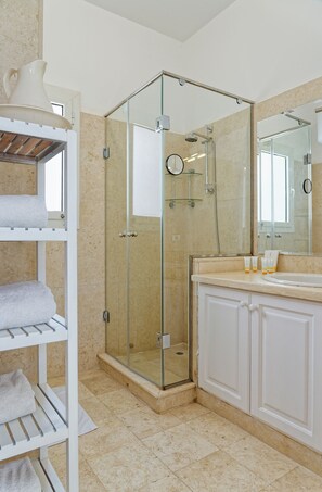 A modern bathroom with a glass-enclosed shower, a white vanity with a mirror, and a built-in shelf with towels. - Vesta - Luxury Villa - 5BR - White Villas (El Gouna)