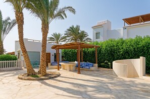 A courtyard with palm trees, a wooden pergola, and outdoor seating. - Vesta - Luxury Villa - 5BR - White Villas (El Gouna)