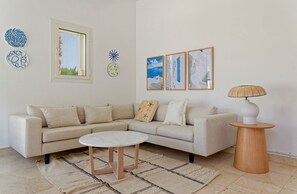 Ein Wohnzimmer mit einem beigen Sofa, einem runden Couchtisch und einer Lampe auf einem Holznachttisch.