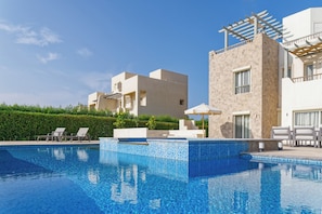 A swimming pool with lounge chairs, a stone building, and a clear blue sky. - Vesta - Luxury Villa - 4BR - Joubal II (El Gouna)