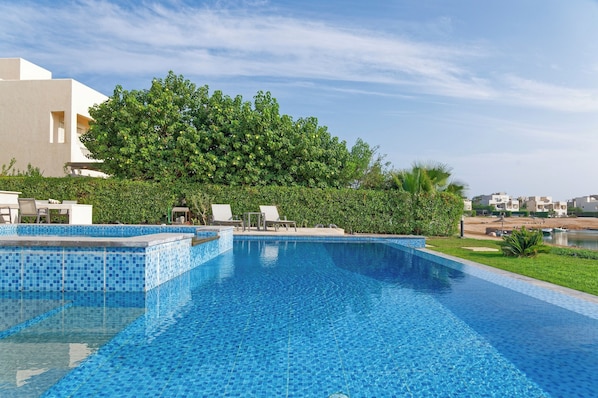 A swimming pool with tiled edges, lounge chairs, and a hedge. - Vesta - Luxury Villa - 4BR - Joubal II (El Gouna)