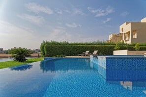 An infinity pool with a clear blue edge, surrounded by a well-maintained hedge and a palm tree. - Vesta - Luxury Villa - 4BR - Joubal II (El Gouna)